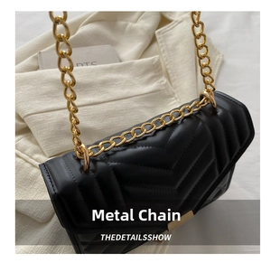 Close-up of black V-quilted faux leather bag with gold chain strap on blazer