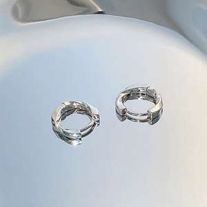 Macro detail of silver twisted hoop earrings with a polished metallic finish on reflective glass