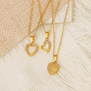 Three elegant gold heart necklaces with zircon inlays on warm textured background