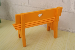 Macro view of a miniature orange wooden bench with a decorative heart-shaped cutout