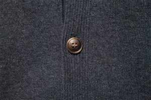 Macro detail of dark grey knit fabric with a premium brown tortoiseshell button