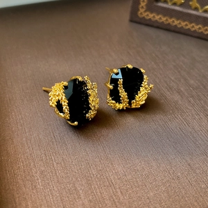 Gros plan de boucles d'oreilles dorées avec une pierre noire et une texture de corail