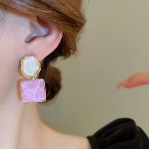 Nahaufnahme geometrischer Goldohrringe mit rosa Marmor und weißem Harz am Modell