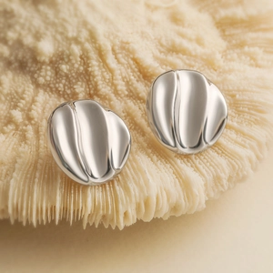 Macro shot of silver plated heart-shaped geometric stud earrings on a coral texture