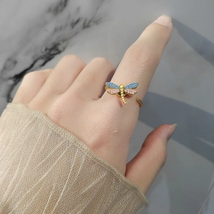 Drehbarer Libellenring mit rosa und blauen Kristallen in Gold auf Marmorhintergrund