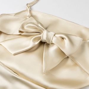 Detail of champagne satin dress featuring a large bow and elegant silk texture