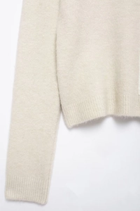 Close-up of the beige knit sweater showing ribbed cuffs and soft textured wool fabric