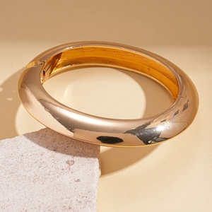 Macro detail of glossy gold chunky cuff bracelet on textured stone podium base