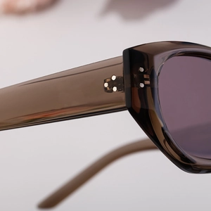 Detailed close-up of warm tea-colored acetate frame with triple metal rivets on the hinge