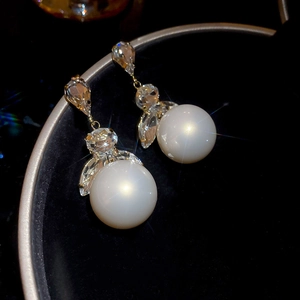 Macro shot of elegant pearl drop earring with tassel crystal detailing on black velvet tray
