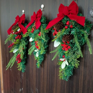 Christmas teardrop wreath with red bow, pine cones and berries on a dark wood door