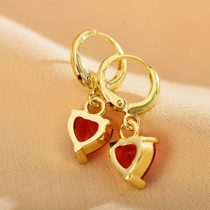 Macro shot of gold hoop earrings with red heart zircon pendants on soft fabric