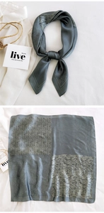 Detail of grey patterned silk scarf showing floral, dot, and wave textures on white fabric