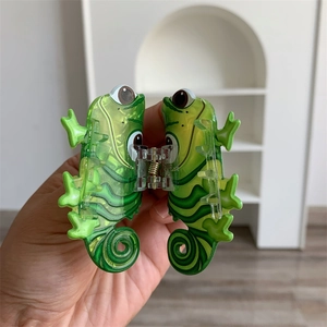 Detailed close-up of a green chameleon acrylic hair claw clip with printed eyes and stripes