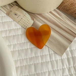 Detail of amber acetate heart hair clip with handmade engraving on white quilted fabric