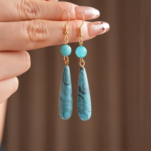 Dettaglio di orecchini a goccia in resina blu con ganci dorati dallo stile vintage retrò