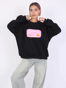 Detail der rosa russischen Text- und Kuhillustration auf einem schwarzen Oversize-Sweatshirt