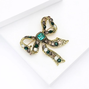 Detail of vintage gold bow brooch featuring green and brown crystals on a white stand