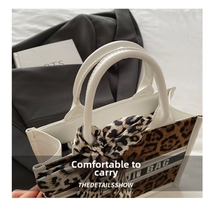 Detailed macro view of leopard print tote bag with white faux leather handles and silk scarf