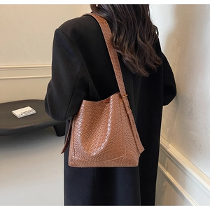 Brown bucket bag with woven texture worn by model over a black winter coat