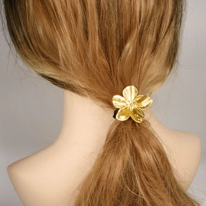 Golden five-petal stainless steel flower hair tie on a model's ponytail with natural lighting