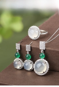 Macro shot of silver jewelry set with white chalcedony and green stone on dark stand