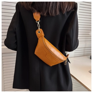 Close-up of brown leather chest bag featuring gold zipper and embossed logo on black suit