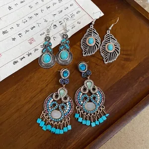 Vintage bohemian turquoise earrings with hollow leaf and tassel details on wood