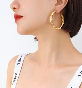 Close-up of elegant gold twisted hoop earrings worn by a model in soft bright lighting