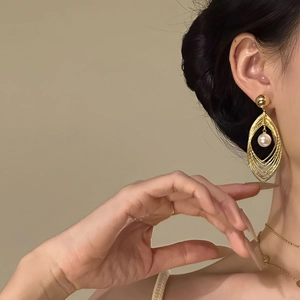 Detail of model wearing layered gold teardrop earrings with a white pearl pendant center