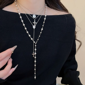 Detail of multi-layer silver cross and pearl necklace set on female model neck