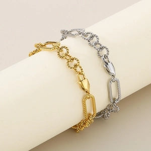 Detail of interlocking gold and silver geometric twisted chain bracelets on a beige pedestal