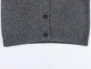 Close-up of ribbed hem and matte black buttons on grey metallic thread knit cardigan