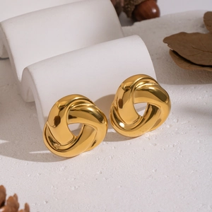 Close-up of golden stainless steel spiral earrings on a white textured stone background