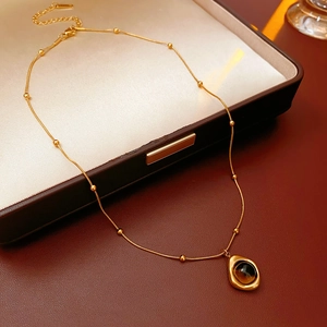 Detail of tiger eye teardrop pendant on gold snake chain with bead accents over leather