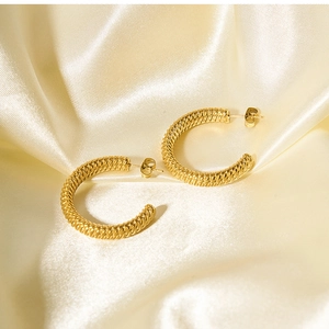 Close-up of golden twisted rope hoop earrings on soft beige silk fabric background
