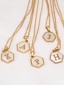 Primer plano de colgantes de letras hexagonales de oro 18K con nácar blanco sobre tela