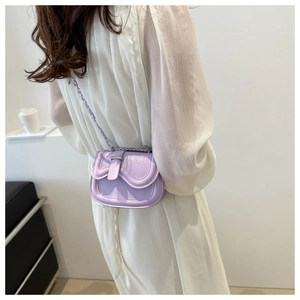 Close-up of purple leather saddle bag with gold chain strap on beige pleated dress