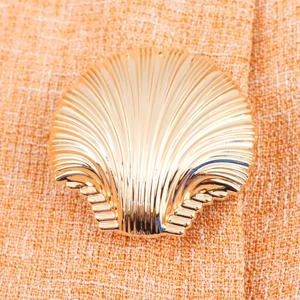 Bouton doré en forme de coquillage sur un ensemble gilet et jupe en tweed orange