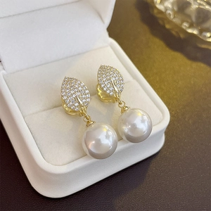 Macro shot of gold leaf earrings with micro-set zircons and a glossy white round pearl