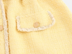 Detailed macro view of yellow tweed fabric with gold textured button and woven braid trim