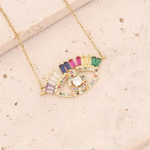 Gold evil eye necklace featuring colorful cubic zirconia on a textured beige stone surface