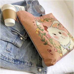 Pink canvas tote bag with rabbit embroidery and striped handles on denim jacket