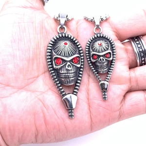 Vintage steel skull pendants with red eyes and zipper detail shown on a palm