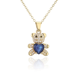 Détail macro du pendentif ourson doré avec gemme de cœur bleu et accents de zircon
