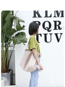Close-up of a large capacity beige checkered canvas shoulder bag worn by a model