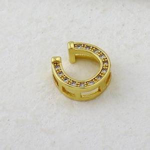 Close-up of golden C-shaped ear cuff with pave cubic zirconia on textured background