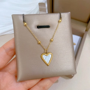 Close-up of a gold heart necklace featuring white mother of pearl inlay and beaded chain