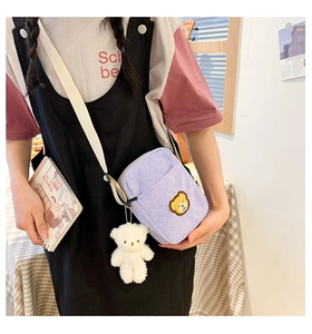 Detail of light purple corduroy crossbody bag featuring a cute yellow bear patch and plush charm