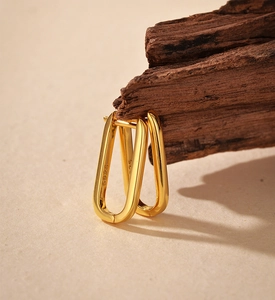 Close-up of minimalist gold S925 sterling silver U-shaped earrings on a wooden block